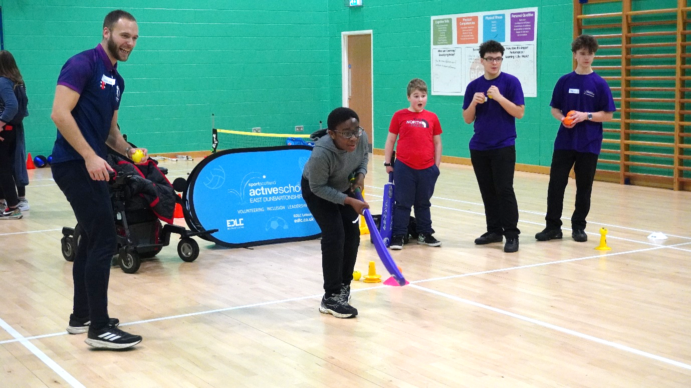 a group of young boys gather round a man with a clip board and football 
